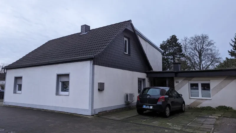 Ein Einfamilienhaus mit Nebengelass und einem PKW davor.