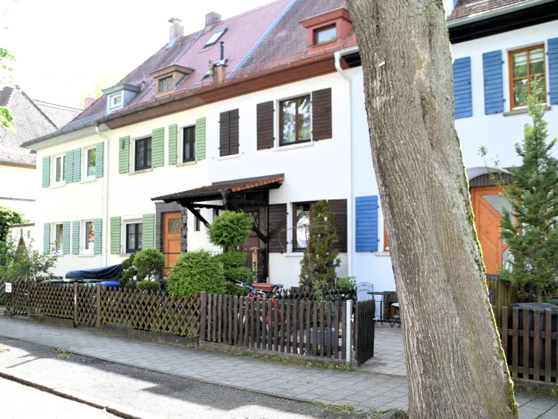 Ein weißes Haus hinter einem Gartenzaun, davor steht ein Baum.