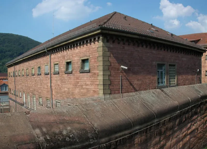 Ein rotes Gefängnisgebäude hinter einer Mauer.