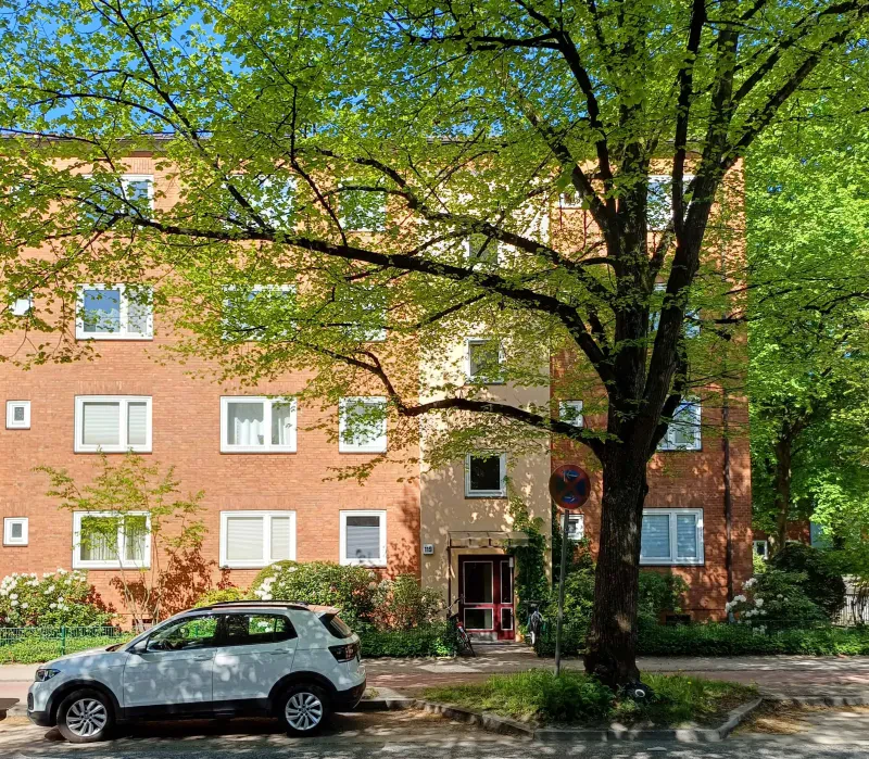 Ein mehrstöckiges rotes haus, davor ein großer Baum und ein parkendes weißes Auto.