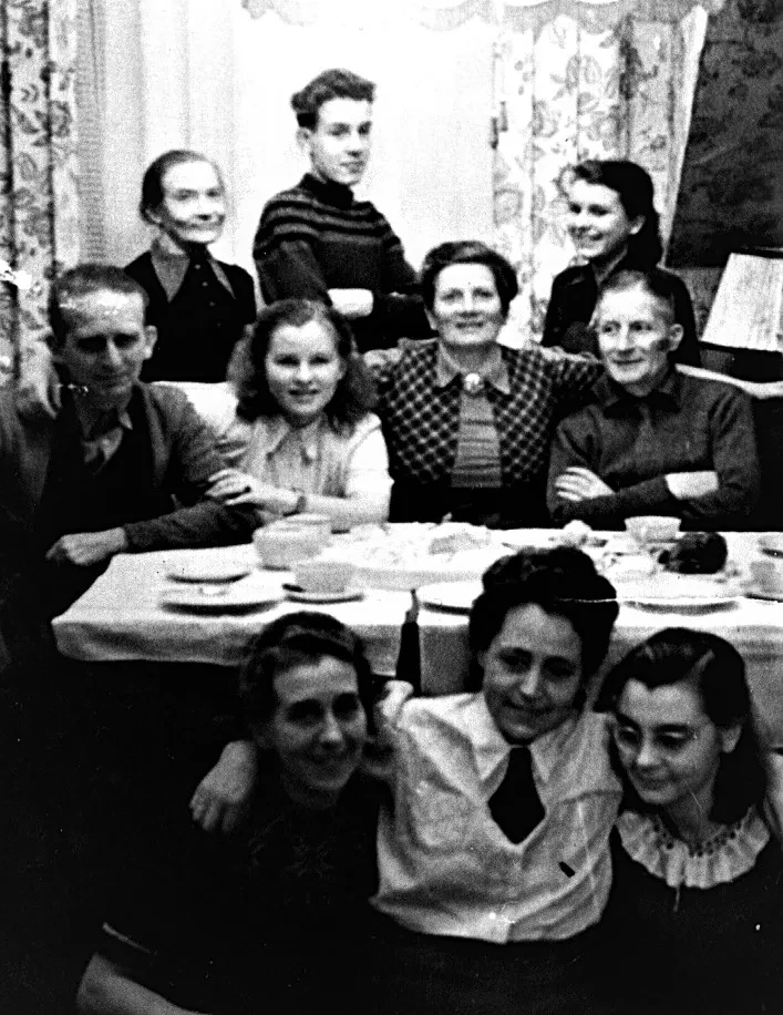 Zehn Personen unterschiedlichen Alters sitzen vor und hinter einer gedeckten Kuchentafel.