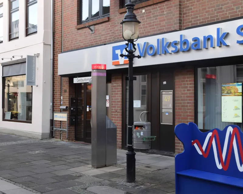 Ein Backsteingebäude mit einem Geldautomaten. Über dem Eingang die Aufschrift „Volksbank“, vor dem Eingang ein Stolperstein.