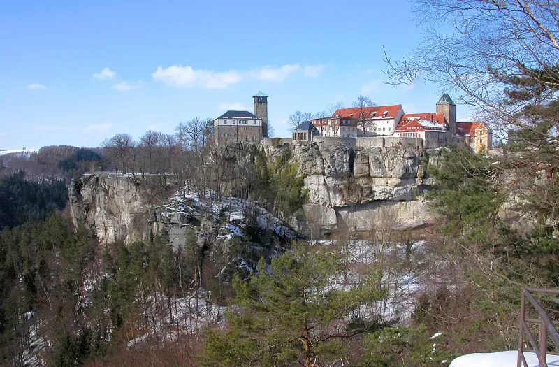 Eine leichte Schneedecke liegt über einem steilen Hang auf dem eine Burg mit Gebäuden aus verschiedenen Jahrhunderten tront.