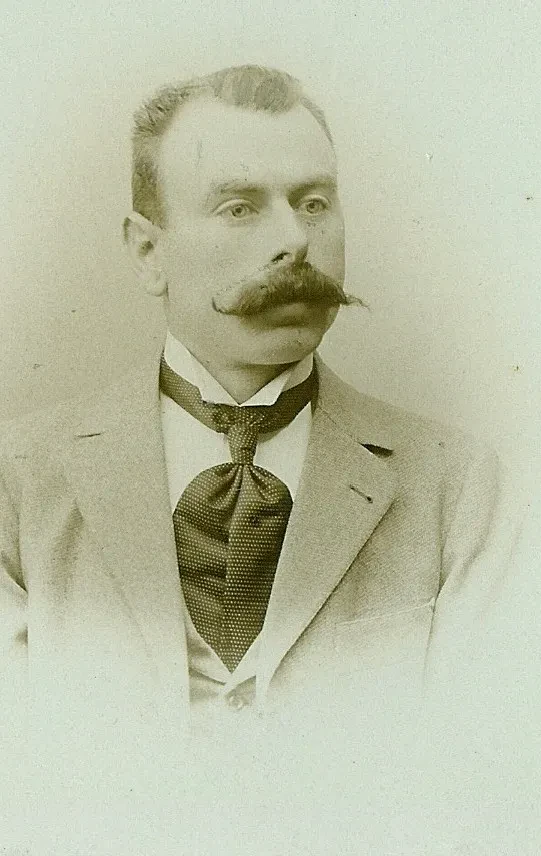 Potrait eines Mannes mit gezwirbeltem Schnurrbart in Anzug und Krawatte.