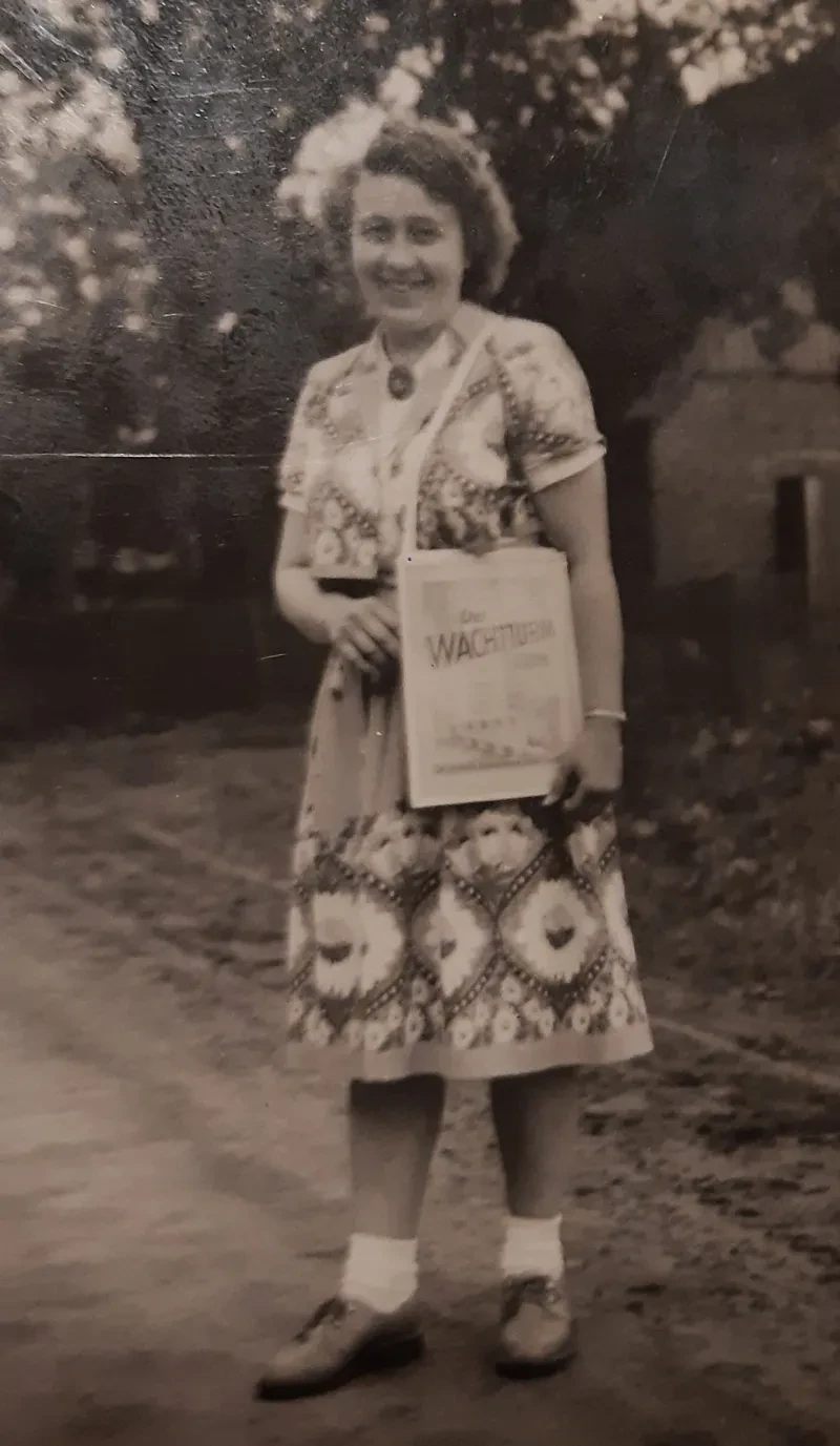 Eine Frau im Kleid trägt eine Umhängetasche auf der das Titelbild der Zeitschrift "Der Wachtturm" zu sehen ist.