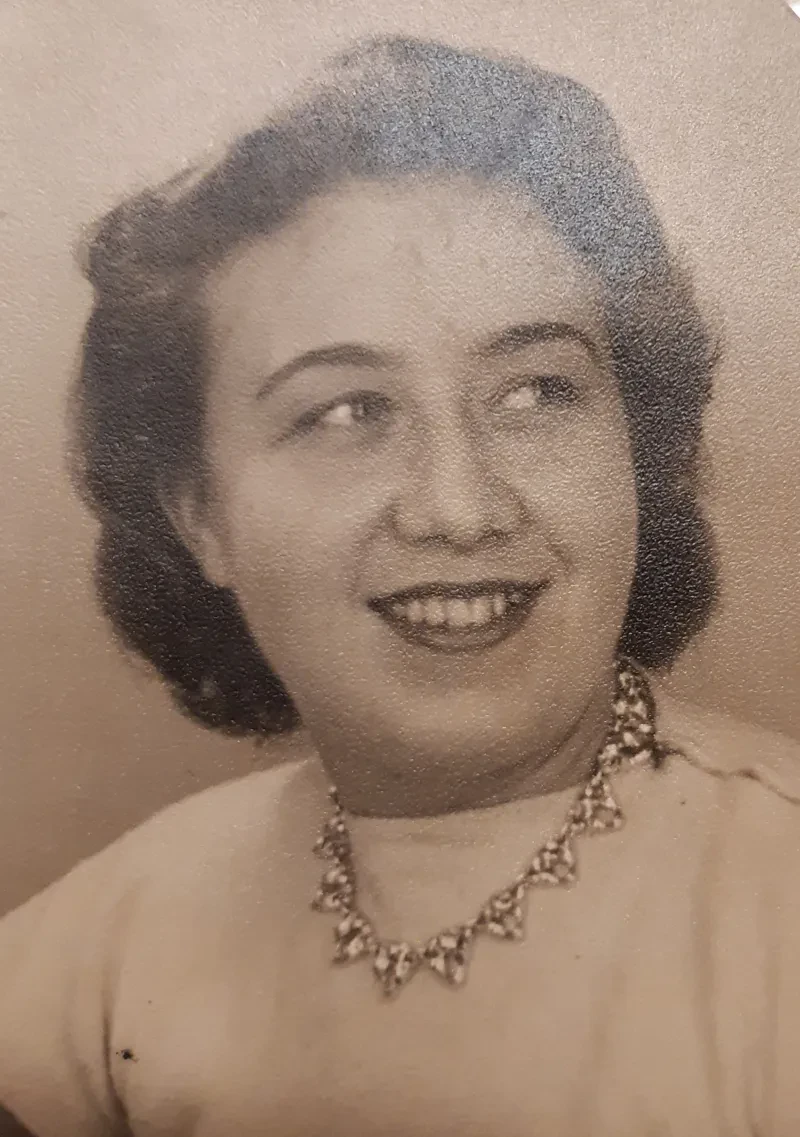 Portrait einer Frau mit einer Kette, die lächelnd seitlich an der Kamera vorbei schaut.