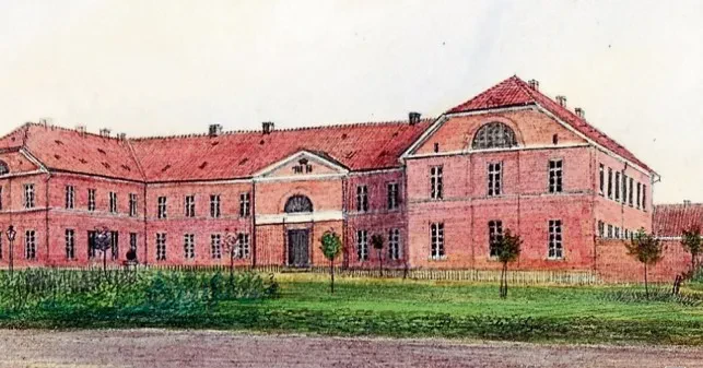 EIn zweistöckiges rotes im Hufeisenform angeordnetes Backsteingebäude mit hohen, schmalen Fenstern.