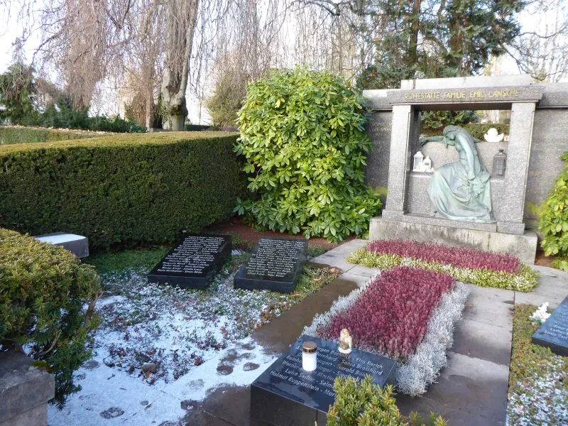 Eine Grabanlage mit verschiedenen Grabplatten und vielen eingravierten Namen. Eine Skulptur stellt eine trauernde Frau dar, darüber die Inschrift: "Ruhestätte Familie Emil Lansche"