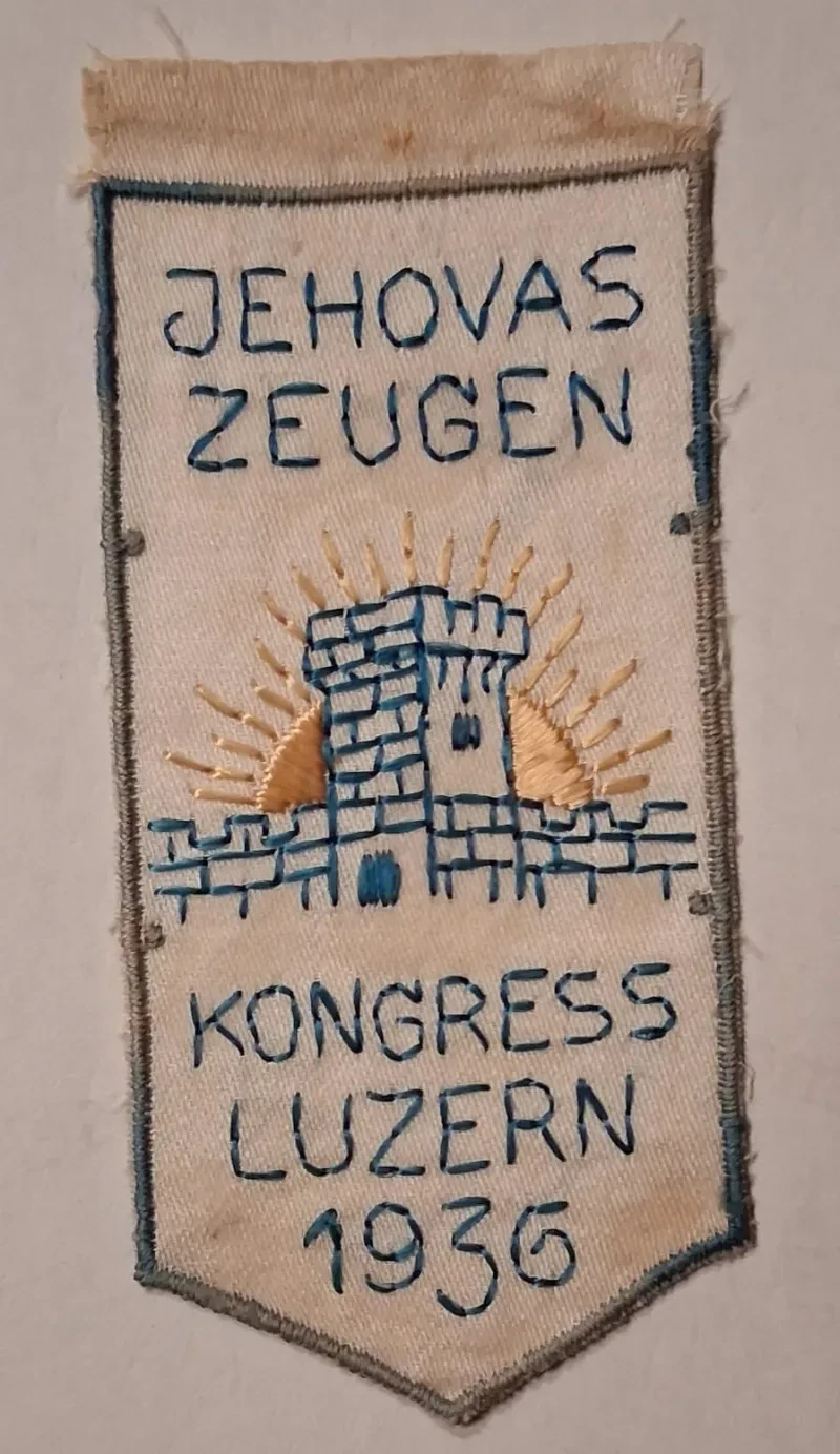 Ein gesticktes Kongressabzeichen mit einem Wachtturm und einer aufgehenden Sonne dahinter sowie der Aufschrift: Jehovas Zeugen Kongress Luzern 1936