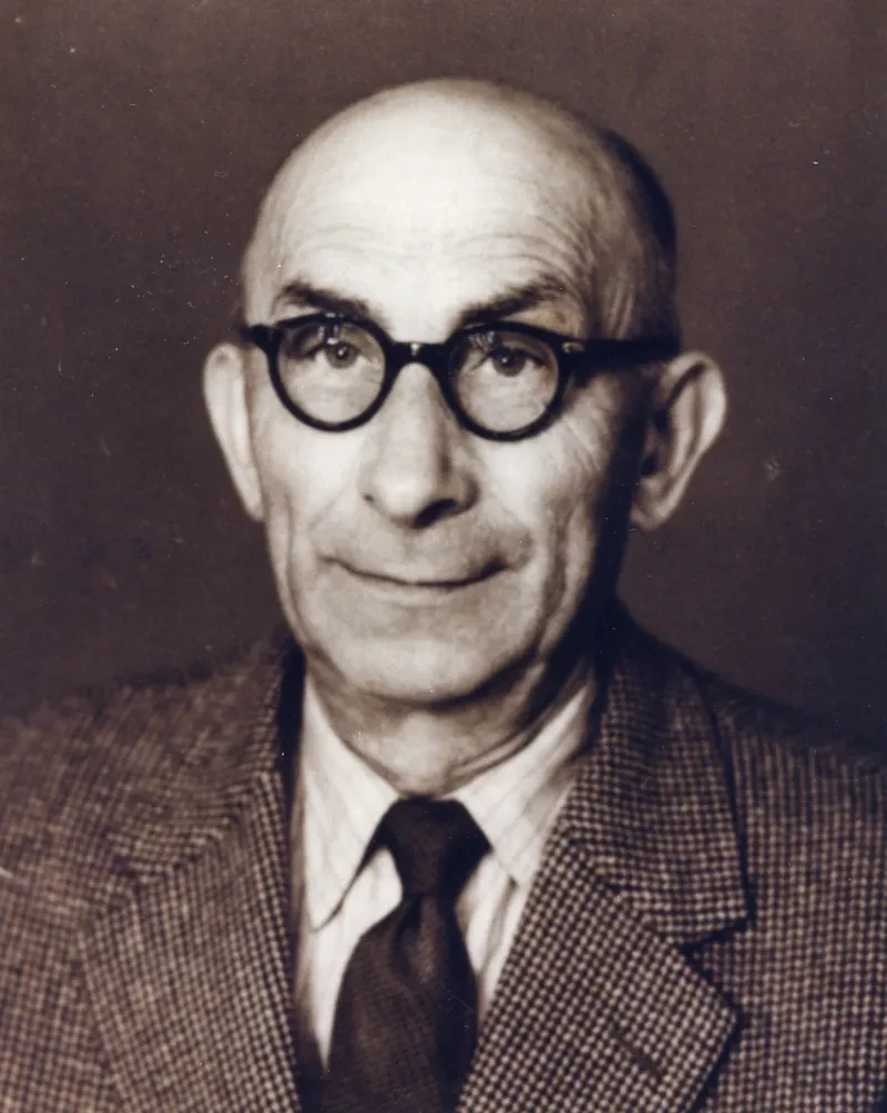 Ein älterer Mann mit Brille, Krawatte und Jackett schaut in die Kamera.