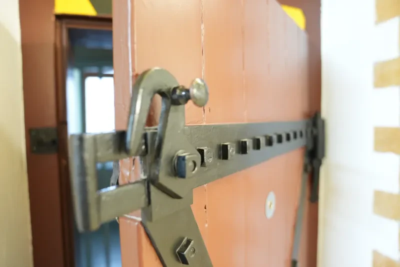Eine hölzerne Tür mit einem großen Metallriegel steht einen Spalt offen.