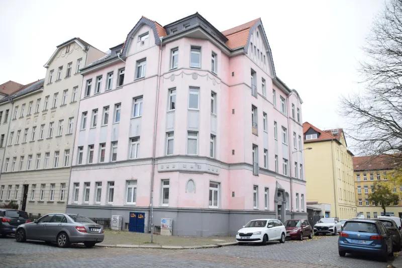 Ein mehrstöckiges Stadthaus, leicht rosa angestrichen an einer Straßenecke, davor parken Autos.