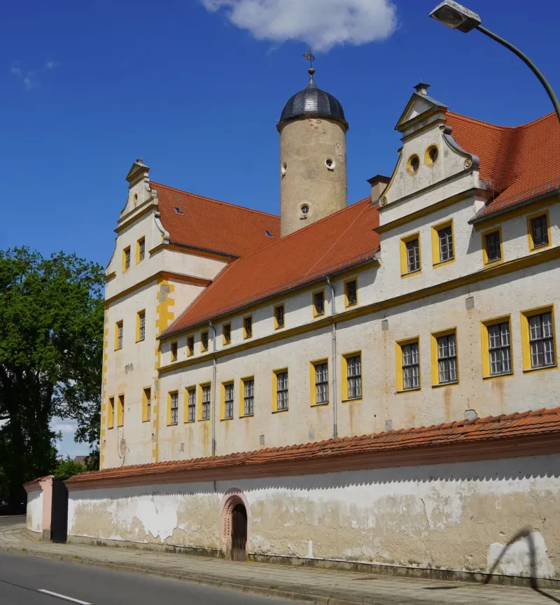 Eine Mauer umgibt ein drei- bis vierstöckiges Schloss mit rotem Dach.