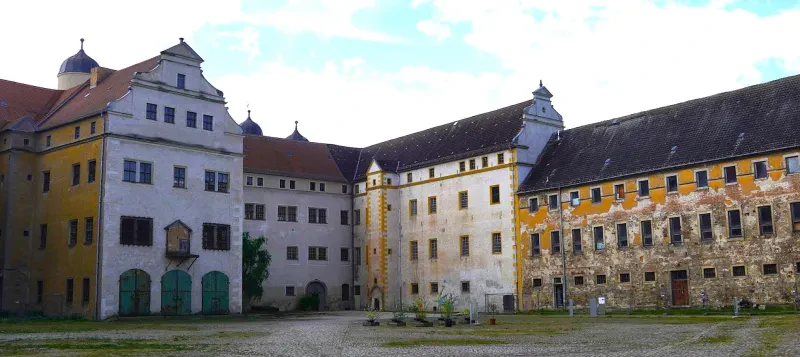 Drei- oder vierstöckige, gelb und weiß verputzte Gebäude aus verschiedenen Zeitepochen umgeben einen großen geflasterten Hof.