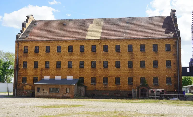 Ein vergittertes, dreistöckiges Backsteingebäude mit Satteldach.