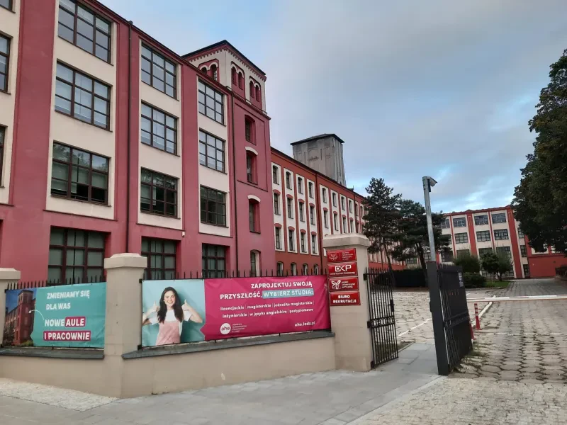 Ein langes, vierstöckiges, rot-weiß gestrichenes Fabrikgebäude mit großen Fenstern und einem L-förmigem Grundriß.