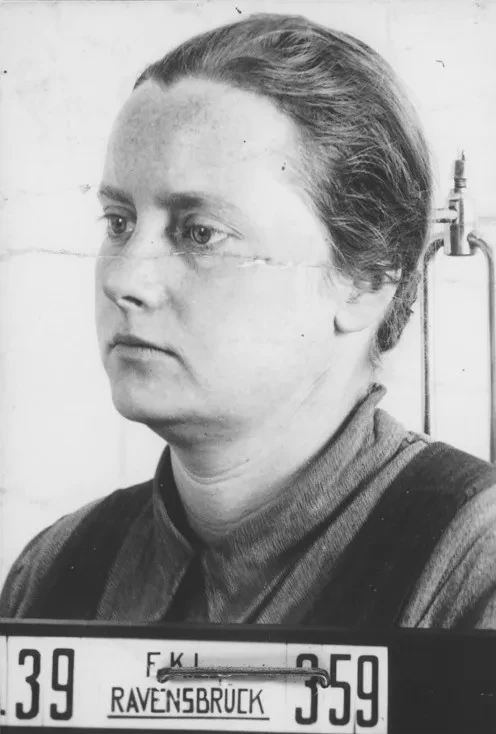 Eine Frau wird fotografiert, vor ihr ein Schild mit der Aufschrift FKL Ravensbrück.