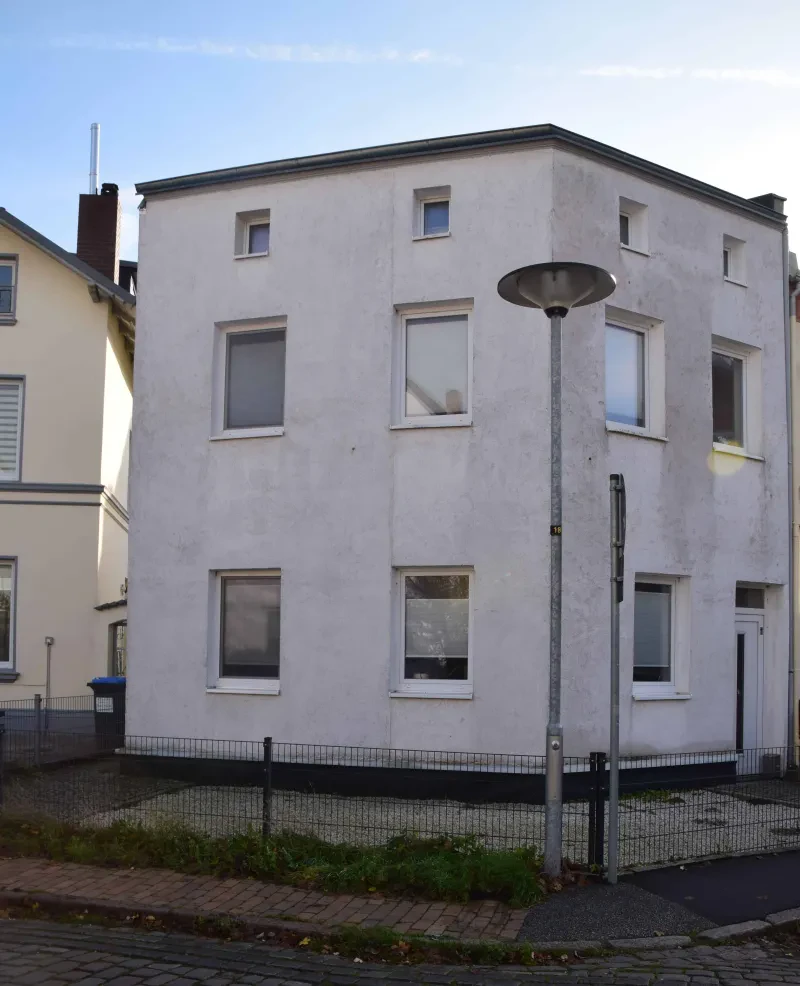 Ein weißes Wohnhaus, davor ein Gehweg und eine Straßenlaterne.