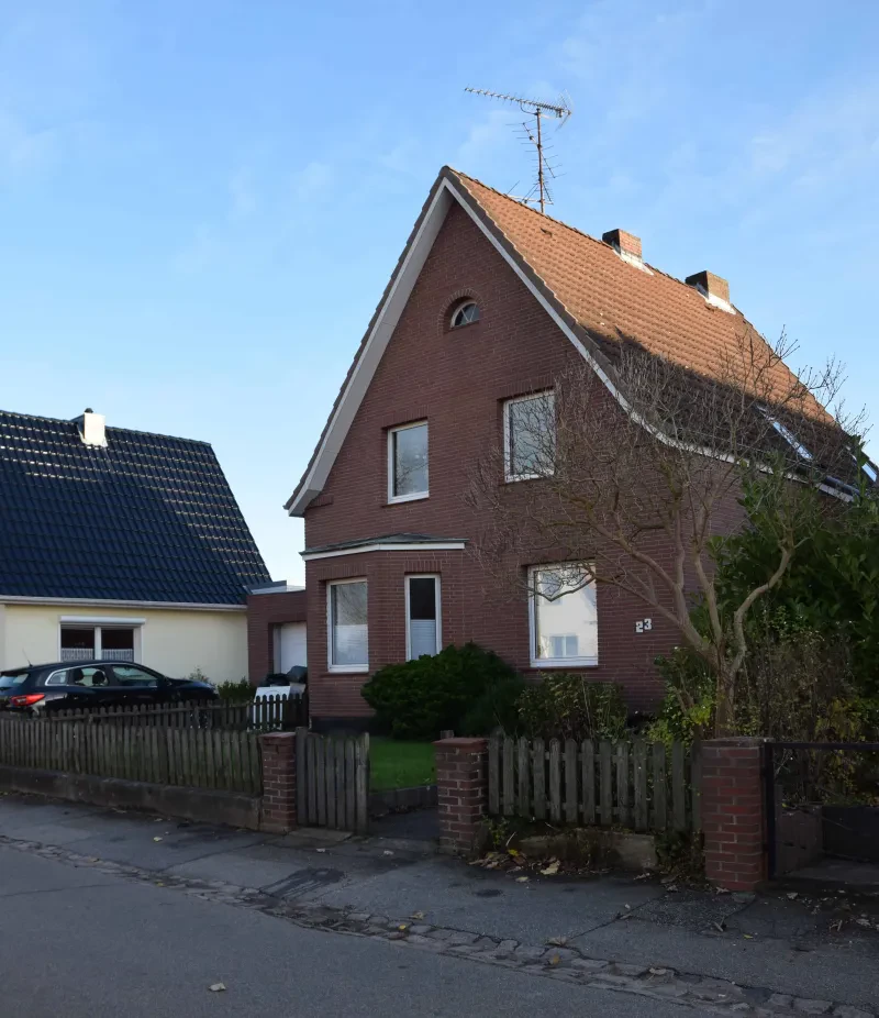 Ein Wohnhaus hinter einem Gartenzaun, vor der Eingangspforte liegt ein Stolperstein.