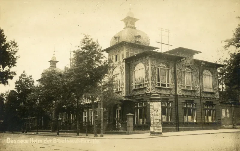 Ein Gebäude an einer Straßenkreuzung, davor eine Litfaßsäule.