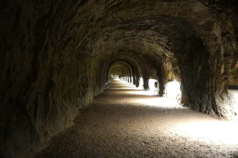 Ein langer in den Fels getriebener Stollen wird heute einseitig durch Lampen erleuchtet.