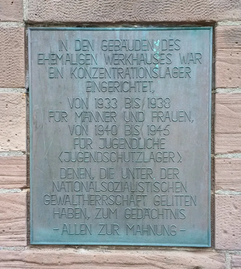 Gedenktafel mit der Aufschrift: "In den Gebäuden des ehemaligen Werkhauses war ein Konzentrationslager eingerichtet, von 1933 bis 1938 für Männer und Frauen, von 1940 bis 1945 für Jugendliche (Jugendschutzlager). Denen, die unter der nationalsozialistischen Gewaltherrschaft gelitten haben, zum Gedächtnis - allen zur Mahnung-"