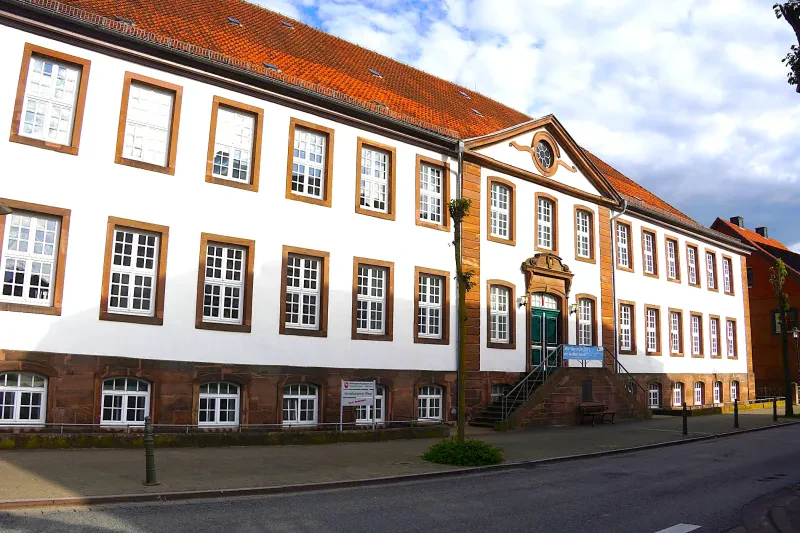 Ein repräsentatives weiß verputztes, langgestrecktes Gebäude mit rotem Dach, dessen Kellergeschoss mit Gewölbefenster aus einer Steinsockelfassade besteht.