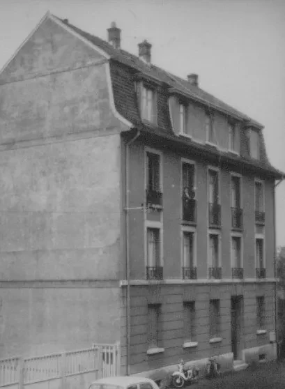 Ein vierstöckiges Wohnhaus, davor stehen verschiedene Fahrzeuge.