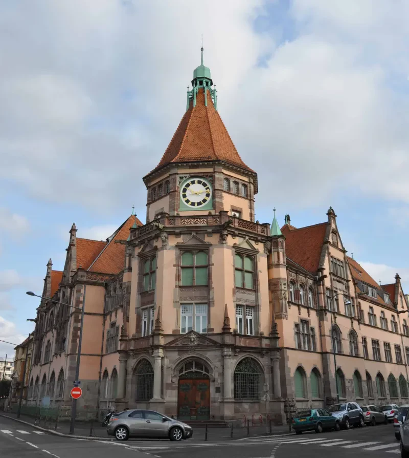 Ein Gebäude an einer Kreuzung mit einem Turm. Davor parkt ein Auto.