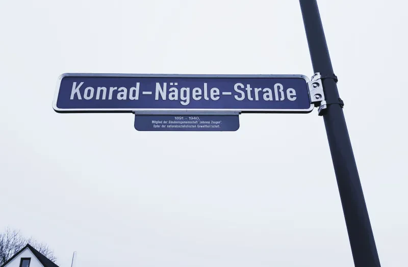 Straßenschild der "Konrad Nägele-Straße" mit dem Zusatzschild "1891-1940, Mitglied der Glaubensgemeinschaft "Jehovas Zeugen", Opfer der nationalsozialistischen Gewaltherrschaft."