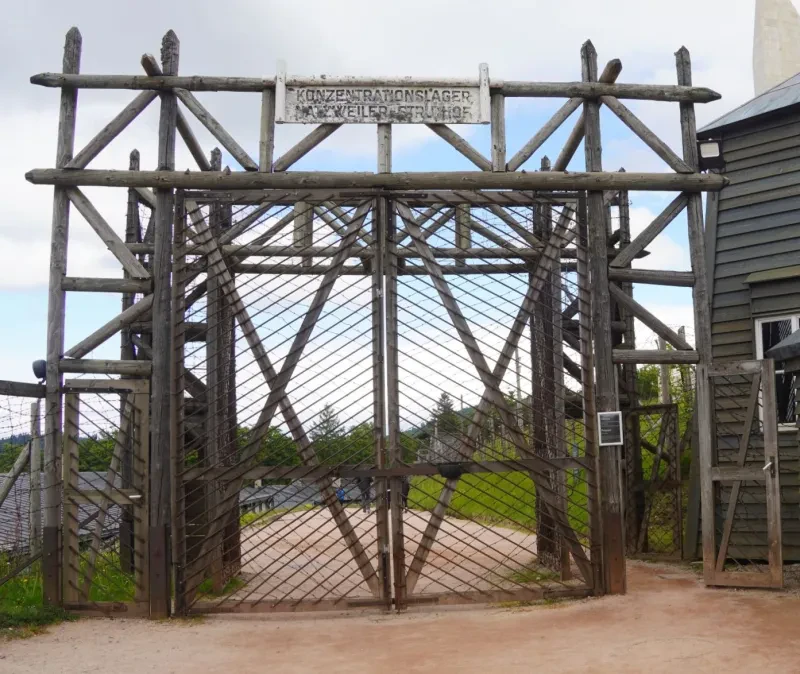Ein doppelflügeliges Tor aus Holzfachwerk, welches durch Draht verstärkt ist steht neben einem einstöckigem Torgebäude und einem Wachturm.