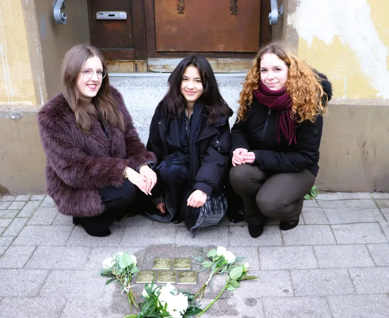Drei Mädchen hinter den fünf Stolpersteinen stehend bzw. hockend.