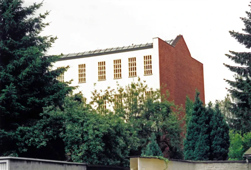 Blick auf ein Gebäude mit vergitterten Fenstern, davor Bäume.