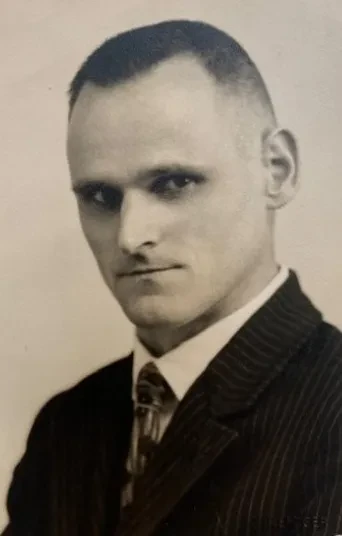 Portrait eines ernst blickenden Mannes im mittleren Alter mit Anzug und Krawatte.