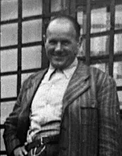 Ein kräftiger, älterer Herr mit lichtem Haar ist in Hemd und Jacket gekleidet.