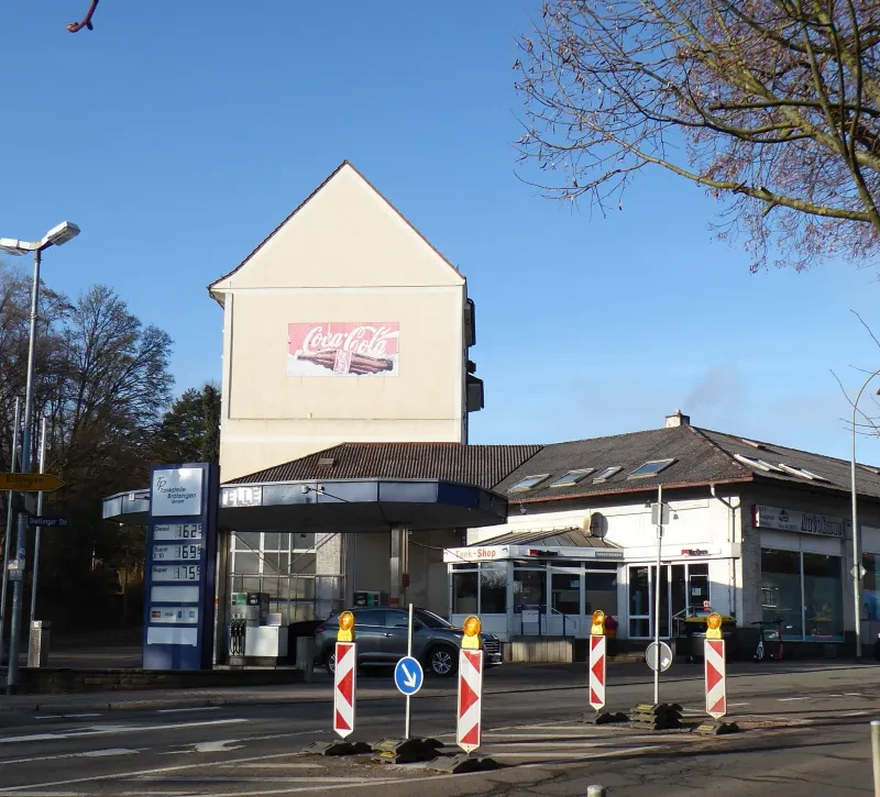 Eine Tankstelle hinter einer Straße, an einer Giebelwand eine Coca-Cola-Werbung.