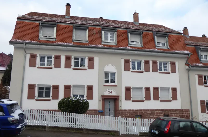 Ein zweistöckiges haus hinter einem weißen Zaun. Davor parken zwei Autos.