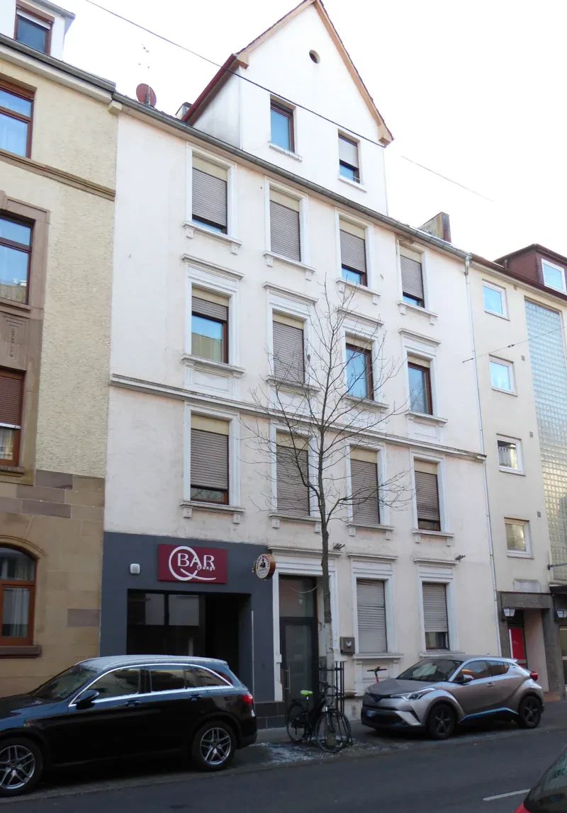 Ein mehrstöckiges Haus, davor parken Autos und ein Fahrrad.