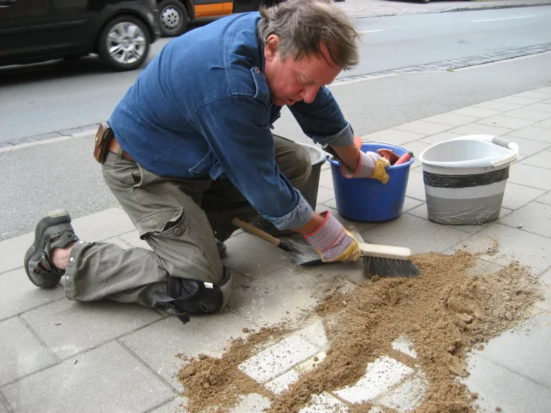 Der Künstler Gunter Demnig fegt nach der Verlegung des Stolpersteins für Bertha Heinsius den Sand vom Stein.