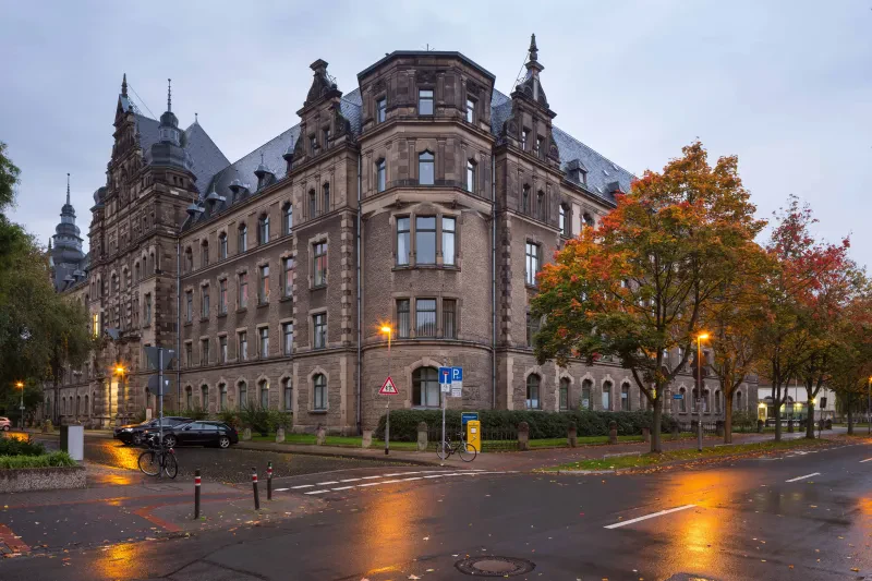 Das Polizeipräsidium an einer Kreuzung am Abend, die Straßenlaternen sind angeschaltet.