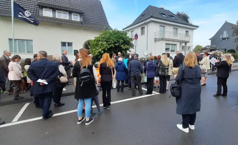 Eine Gruppe Zuschauer steht während der Stolpersteinverlegung im Halbkreis um das Wohnhaus des Ehepaars Guth. Rechts im Bild steht das Fahrzeug des Bauhofs, der Stadt Radevormwald, der die Verlegung durchführte.