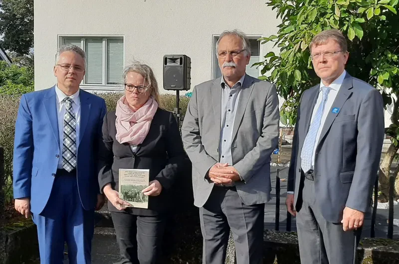 Die vier Redner der Stolpersteinverlegung stehen vor dem ehemaligen Wohnhaus des Ehepaars Guth. Frau Kausemann hält ein Buch über die Verfolgung von Jehovas Zeugen im Bergischen Land in der Hand. Im Hintergrund steht ein Lautsprecher, mit dem die Veranstaltung übertragen wurde.