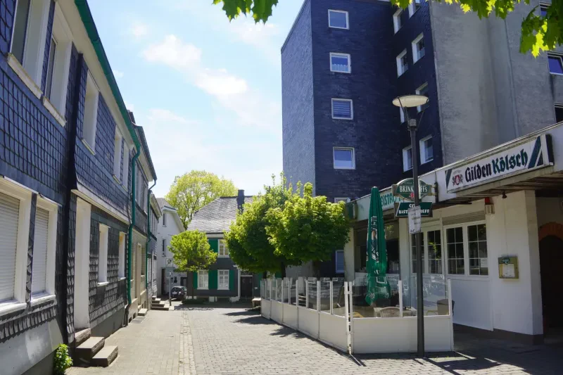 Eine kurze Straße wird auf beiden Seiten von bergischen Schieferhäusern gesäumt. Im Hintergrund rechts steht ein neueres höheres Gebäude.