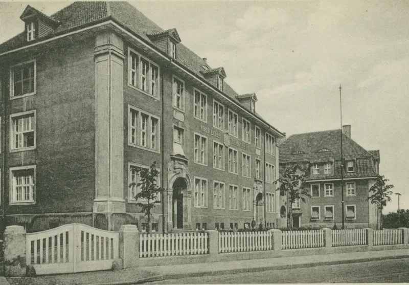 Gebäude von der Seite, umgeben von einem weißen Zaun.
