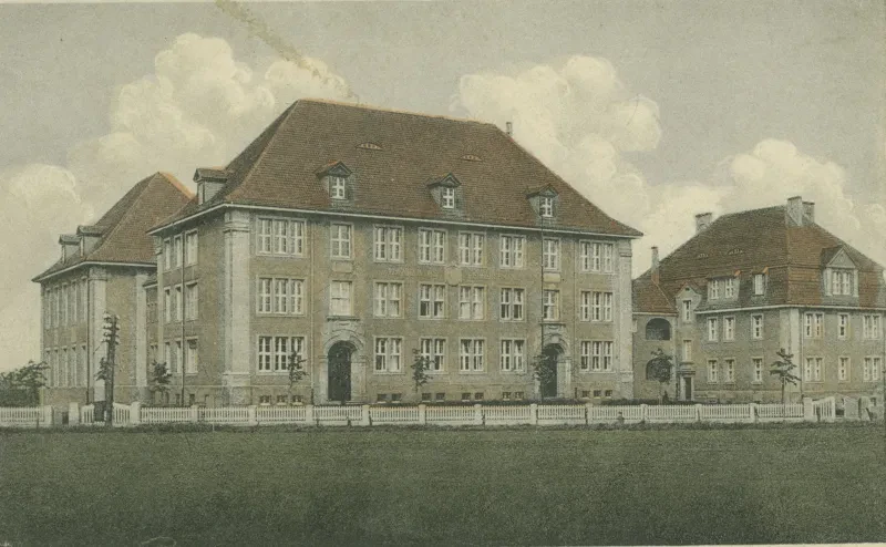 Gebäudekomplex, umgeben von einer grünen Wiese und einem weißen Zaun.