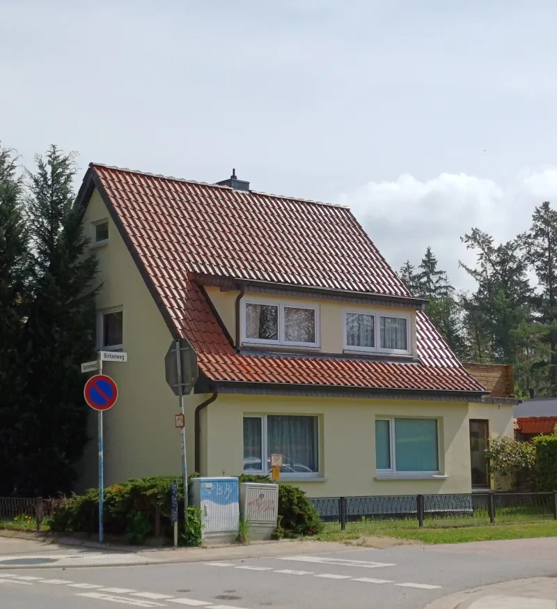 Ein kleines Wohnhaus an einer Straßeneinmündung.