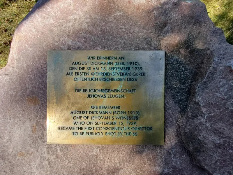 Eine Gedenktafel zur Erinnerung an August Dickmann auf einem Findling auf dem Gelände der Gedenkstätte Sachsenhausen, 1999. Die Tafel enthält den Text: "Wir erinnern an August Dickmann (geb. 1910), den die SS am 15. September 1939 als Wehrdienstverweigerer öffentlich erschießen ließ. Die Religionsgemeinschaft Jehovas Zeugen".
