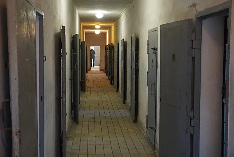 Ein langer Gang mit hellen Fußbodenfliesen und grauen, schweren Holztüren zu beiden Seiten