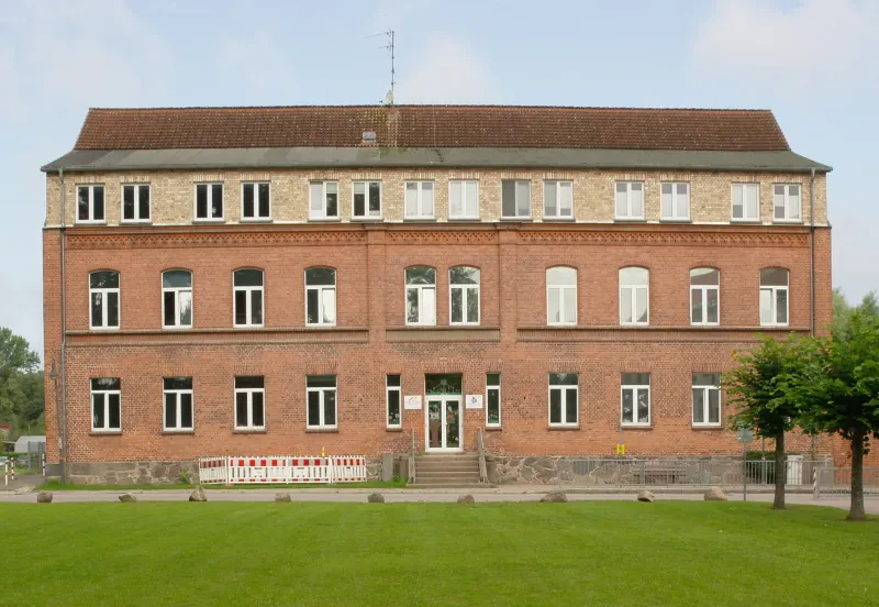 Ein dreistöckiges rotes Backsteingebäude, davor ein grüner Rasen.