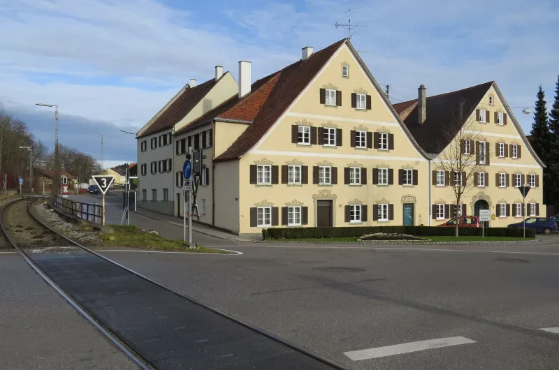 Links im Bild verlaufen Schienen, rechts zwei große Häuser.